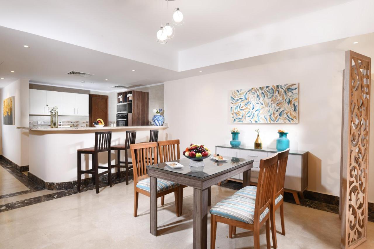 Tolip Resort El Galala Majestic Ain Sukhna Exterior photo The photo shows a modern dining area with a small table and chairs. There is a centerpiece with a bowl of fruit on the table. The room features a light-colored floor and walls, and there is artwork with a colorful design on one wall. In the backgroun