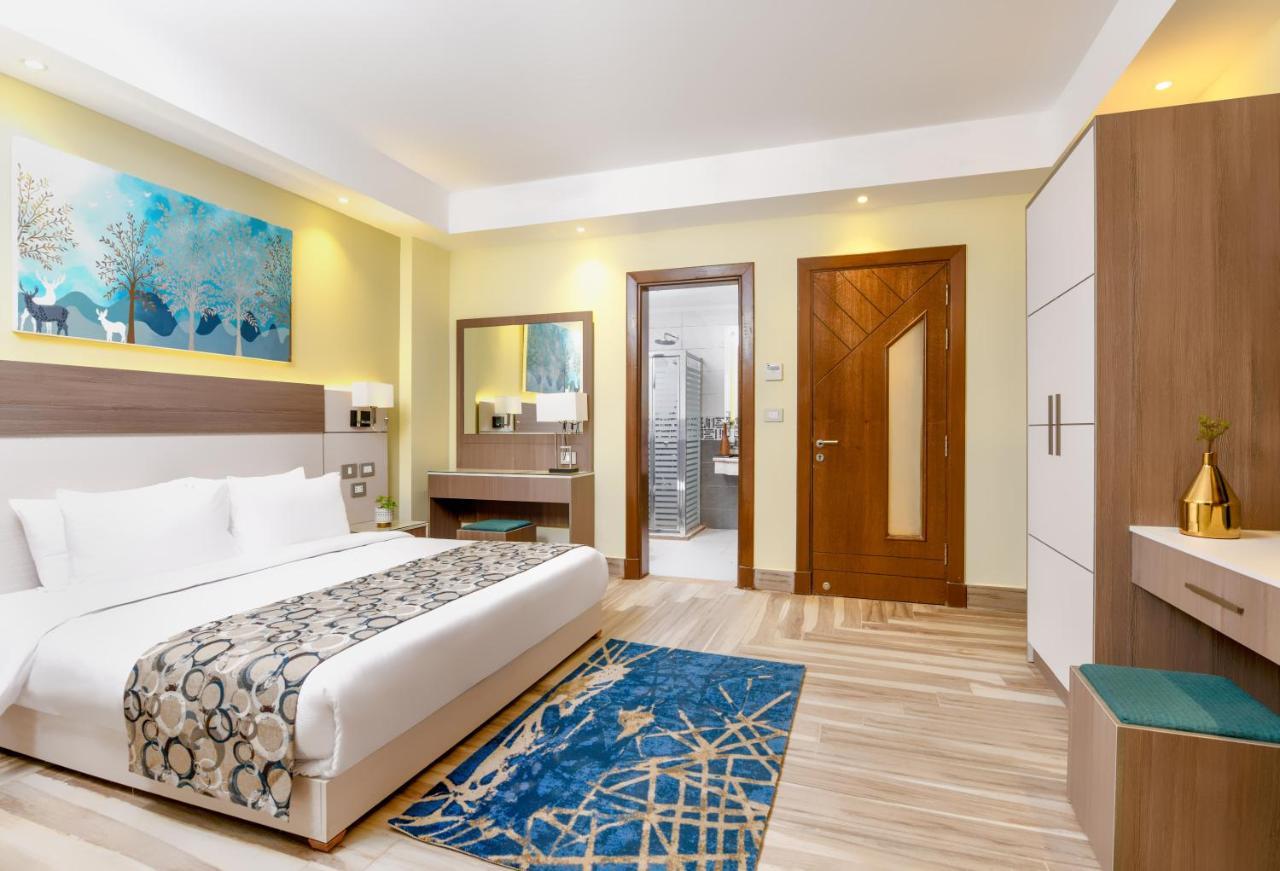 Tolip Resort El Galala Majestic Ain Sukhna Exterior photo The photo shows a well-decorated hotel room. There is a large bed with white linens and a decorative throw blanket. The room features a wooden wardrobe and a bedside table with lamps. A colorful rug is placed on the floor, adding warmth to the space.