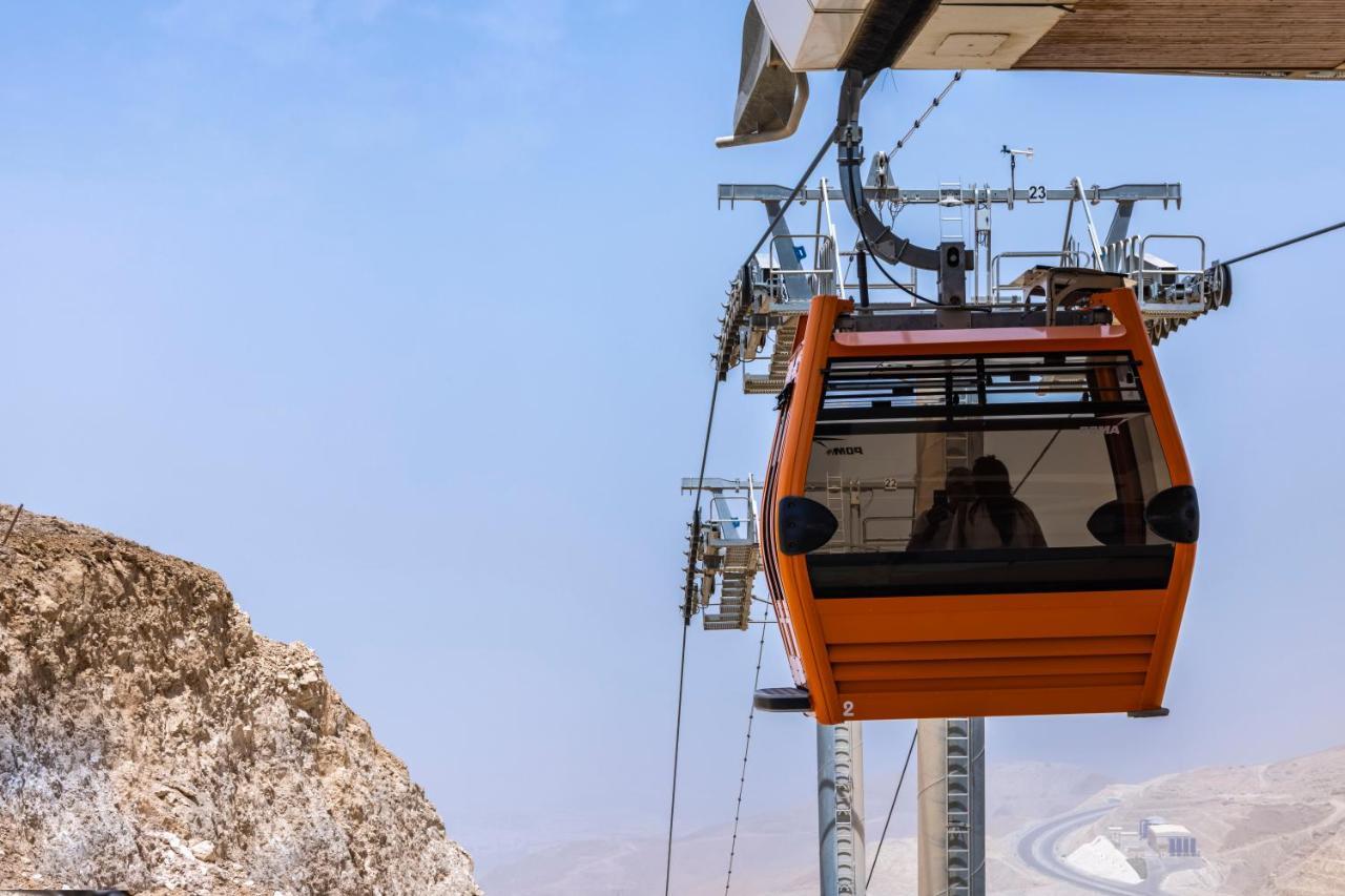 Tolip Resort El Galala Majestic Ain Sukhna Exterior photo The photo shows an orange gondola or cable car hanging on a cable system. The gondola appears to be suspended in the air above a rocky landscape, with a clear sky in the background. There are supporting cables and structures visible, indicating that 