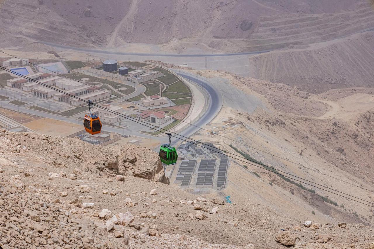 Tolip Resort El Galala Majestic Ain Sukhna Exterior photo The photo shows a scenic view from a high elevation, featuring a cable car system. Two cable cars are visible, one orange and one green, traveling along cables down the mountainside. Below, there appears to be a developed area with roads and light st