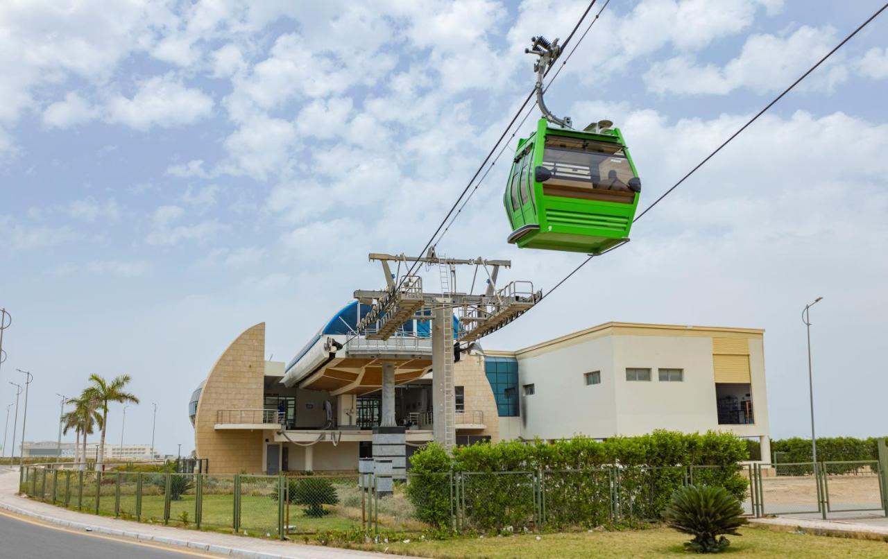 Tolip Resort El Galala Majestic Ain Sukhna Exterior photo The photo shows a cable car or gondola system in operation, featuring a green-colored gondola. It is suspended from cables and moving towards a station, which appears to be a modern building with a unique architectural design. The station has large w