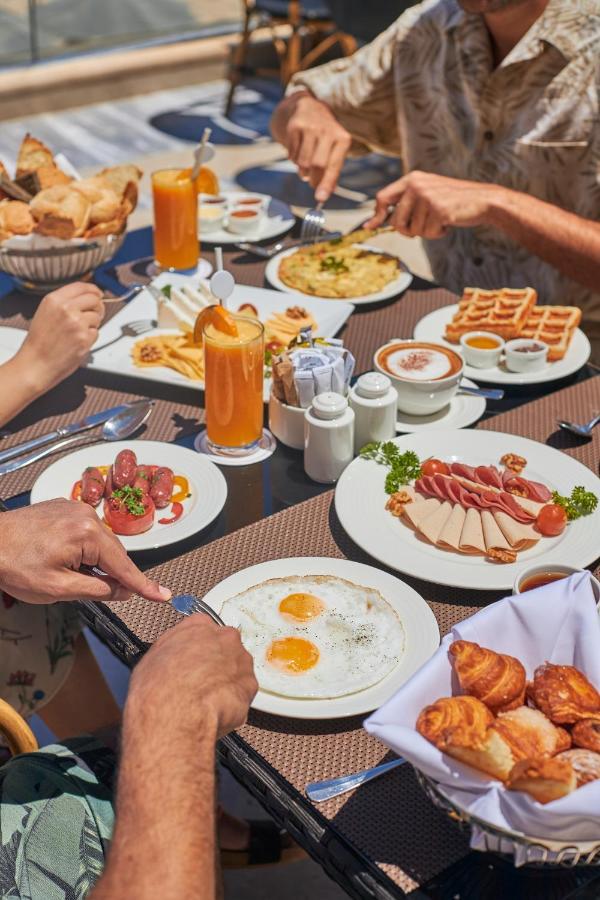 Tolip Resort El Galala Majestic Ain Sukhna Exterior photo The photo features a spread of breakfast dishes on a table. There are two sunny-side-up eggs on one plate, surrounded by various food items, including slices of ham, sausages, and fresh tomatoes. Another plate holds a serving of waffles. A bowl with 