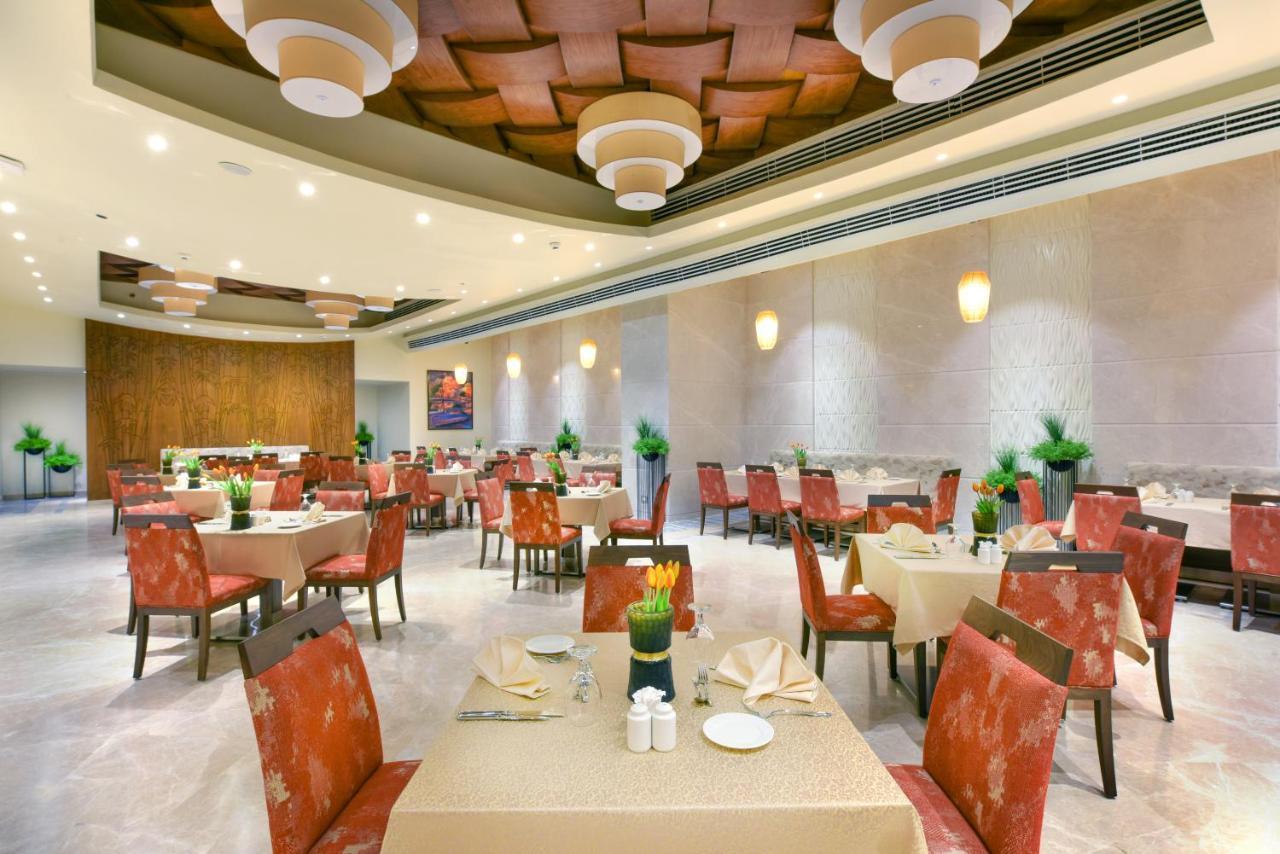 Tolip Resort El Galala Majestic Ain Sukhna Exterior photo The photo shows the interior of a restaurant. The space features several tables set with light-colored tablecloths and chairs with reddish upholstery. Each table is adorned with decorative napkins and has small plants in the center. The room has a mo