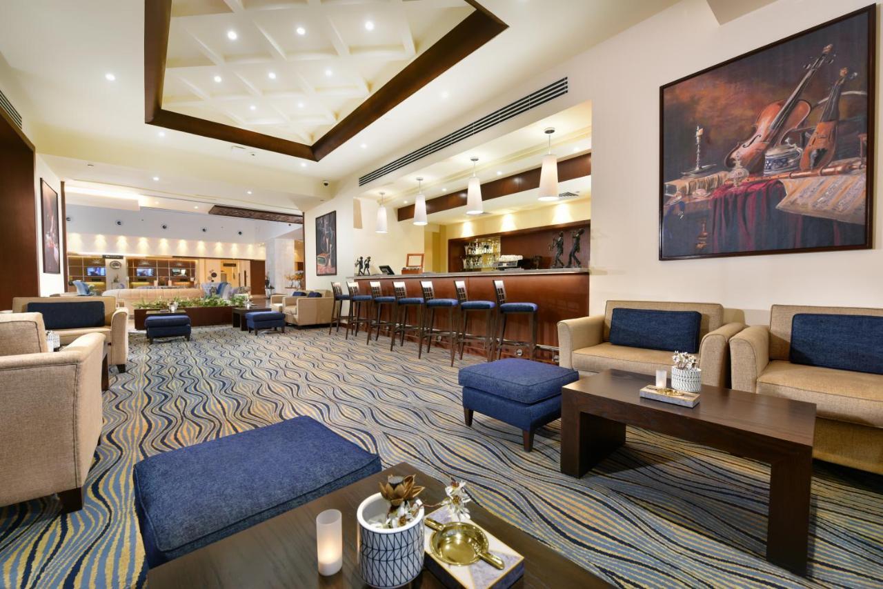 Tolip Resort El Galala Majestic Ain Sukhna Exterior photo The photo depicts a modern, inviting lobby or lounge area. It features a cozy seating arrangement with light-colored sofas and deep blue accent chairs. In the center, there is a low wooden coffee table with decorative items, including a candle and sm