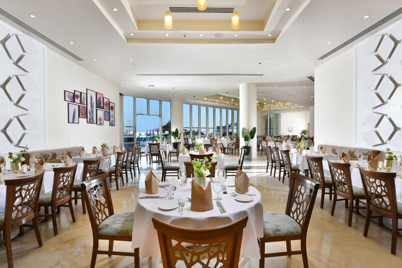 Tolip Resort El Galala Majestic Ain Sukhna Exterior photo The photo displays a spacious and elegantly designed restaurant interior. It features numerous tables set for dining, with white tablecloths, neatly folded napkins, and decorative centerpieces of flowers. The seating consists of wooden chairs that co