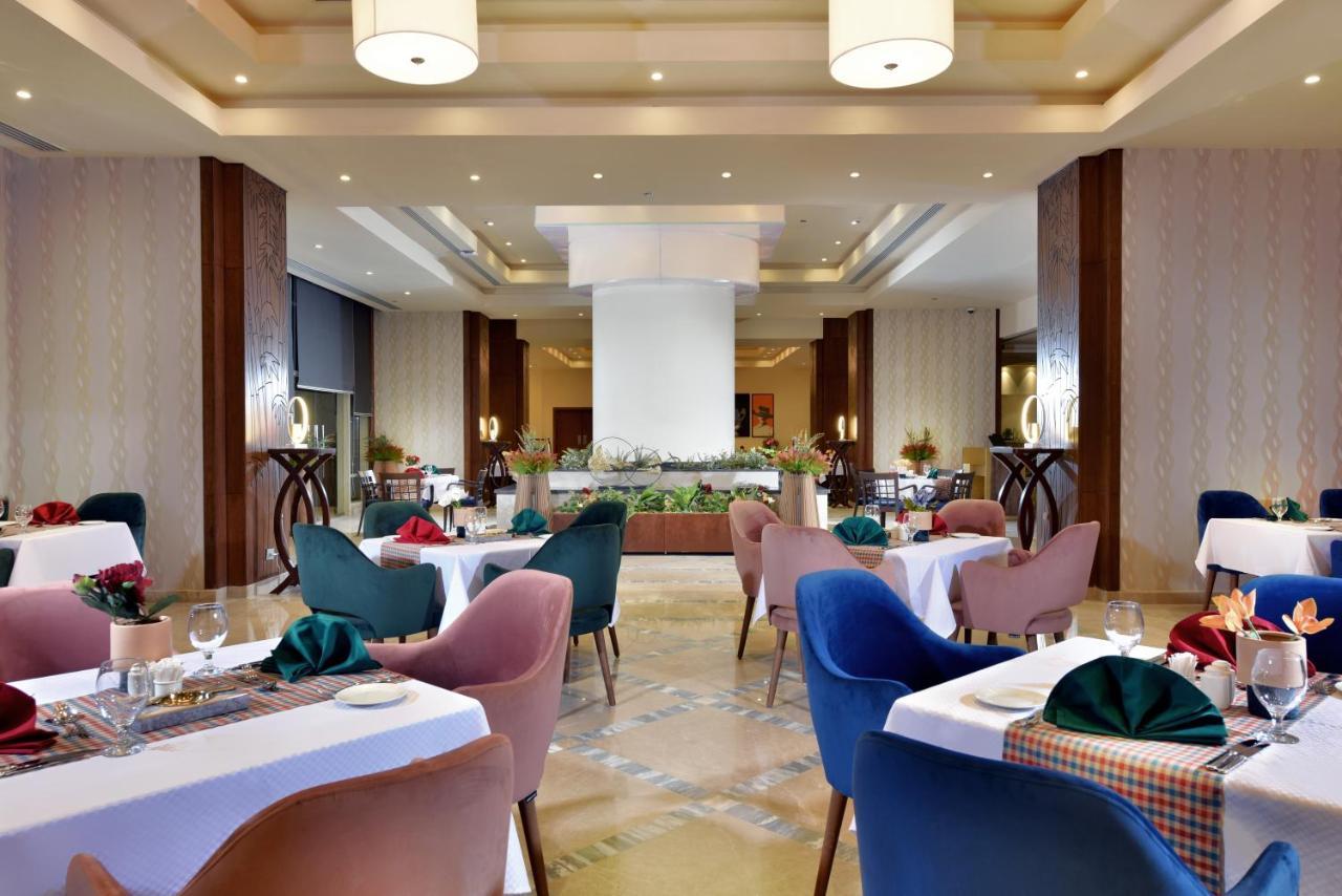Tolip Resort El Galala Majestic Ain Sukhna Exterior photo The photo shows a spacious and elegantly designed restaurant interior. The layout includes several round tables dressed in white tablecloths, each set with decorative plates, cutlery, and colorful napkins. The chairs are upholstered in a variety of c